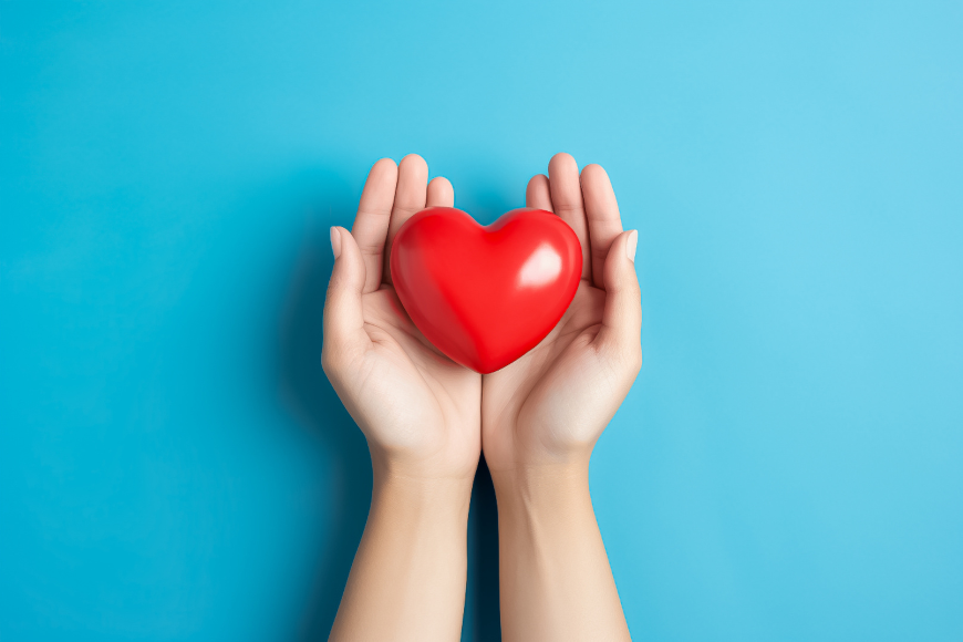 Hands holding a red heart on blue background.