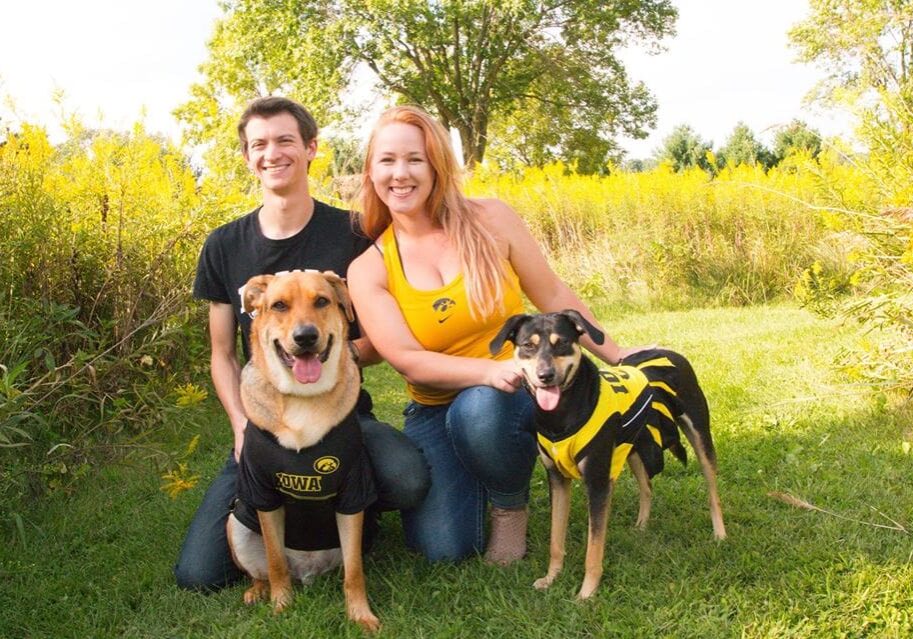 A man and woman pose with their dogs in a field.