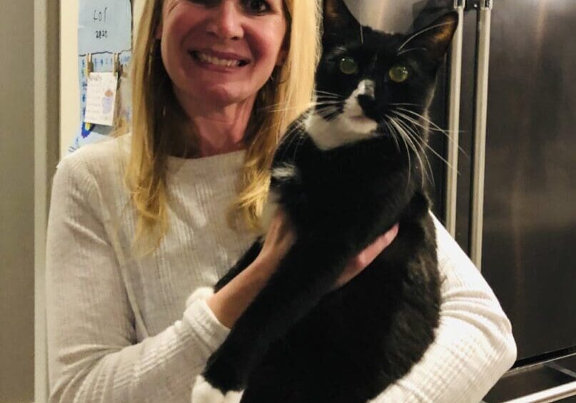 A woman holding a black and white cat in front of a refrigerator.