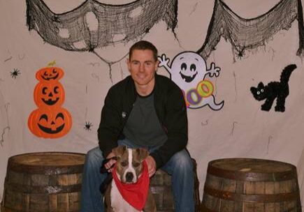 A man with a dog sitting on barrels in front of a halloween backdrop.