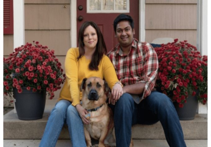 A man and woman sitting on the steps of their home with their dog.