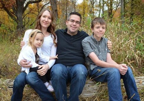 A family sits on a log in a wooded area.