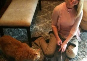 A woman sitting on the floor with two cats.