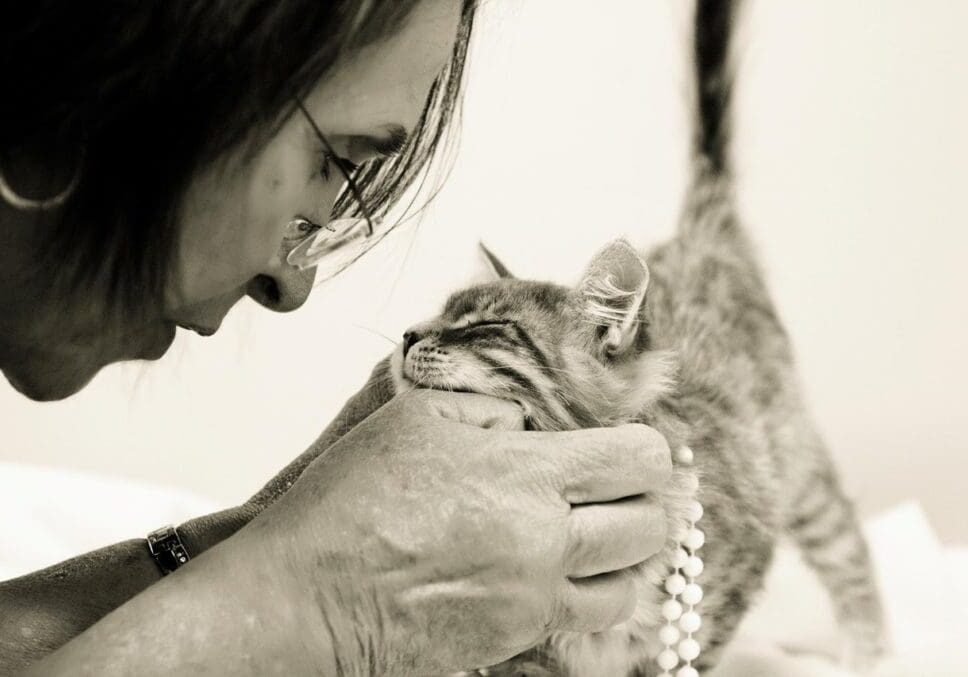 A woman petting a cat with a pearl necklace.