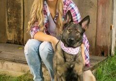 A girl posing with her dog in front of a barn.