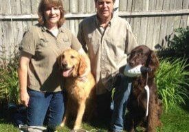 A man and woman posing with their dogs and ducks.