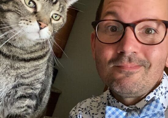 A man wearing glasses and a bow tie with a tabby cat.