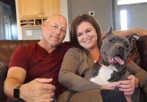 A man and woman sitting on a couch with their dog.