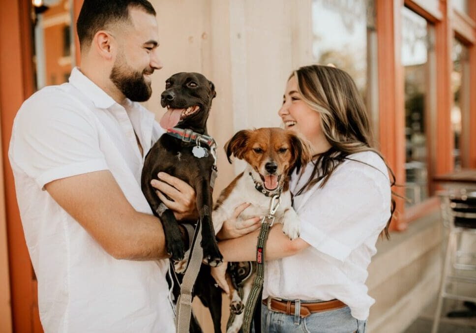 A couple holding their dogs in front of a restaurant.