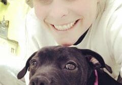 A woman is posing with a black dog.