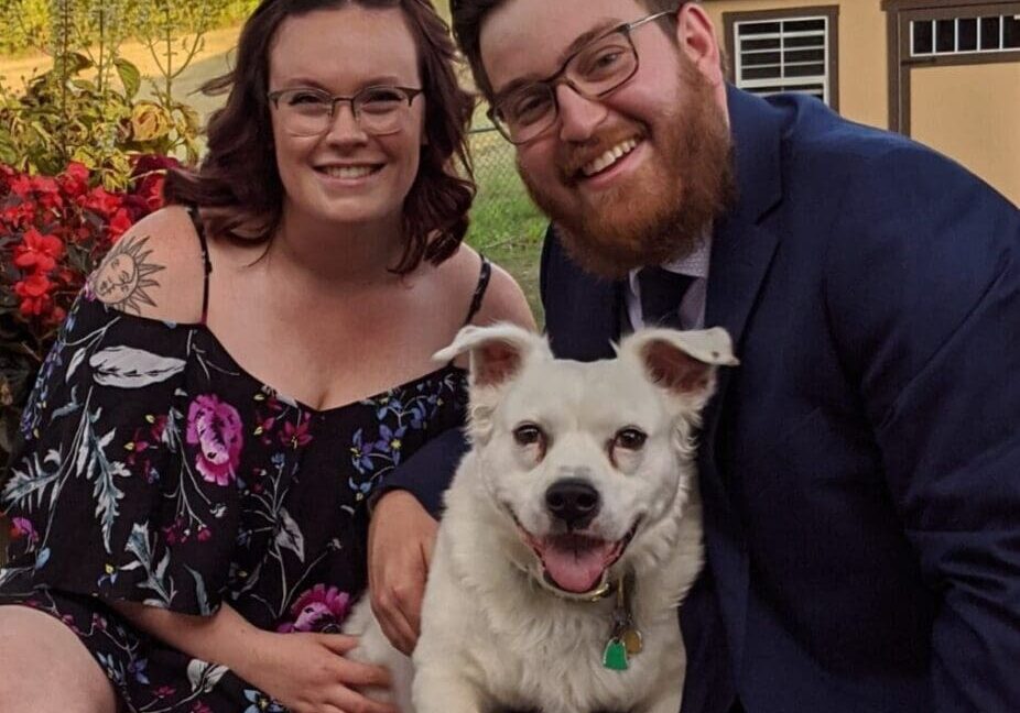 A man and woman pose for a photo with their dog.