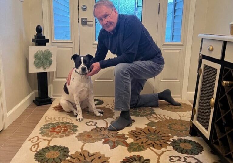 Man kneeling with dog on floral rug.