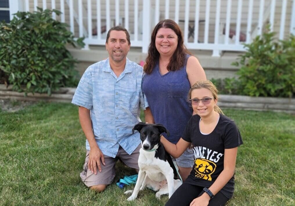 Three people and a dog posing for a photo in front of a house.