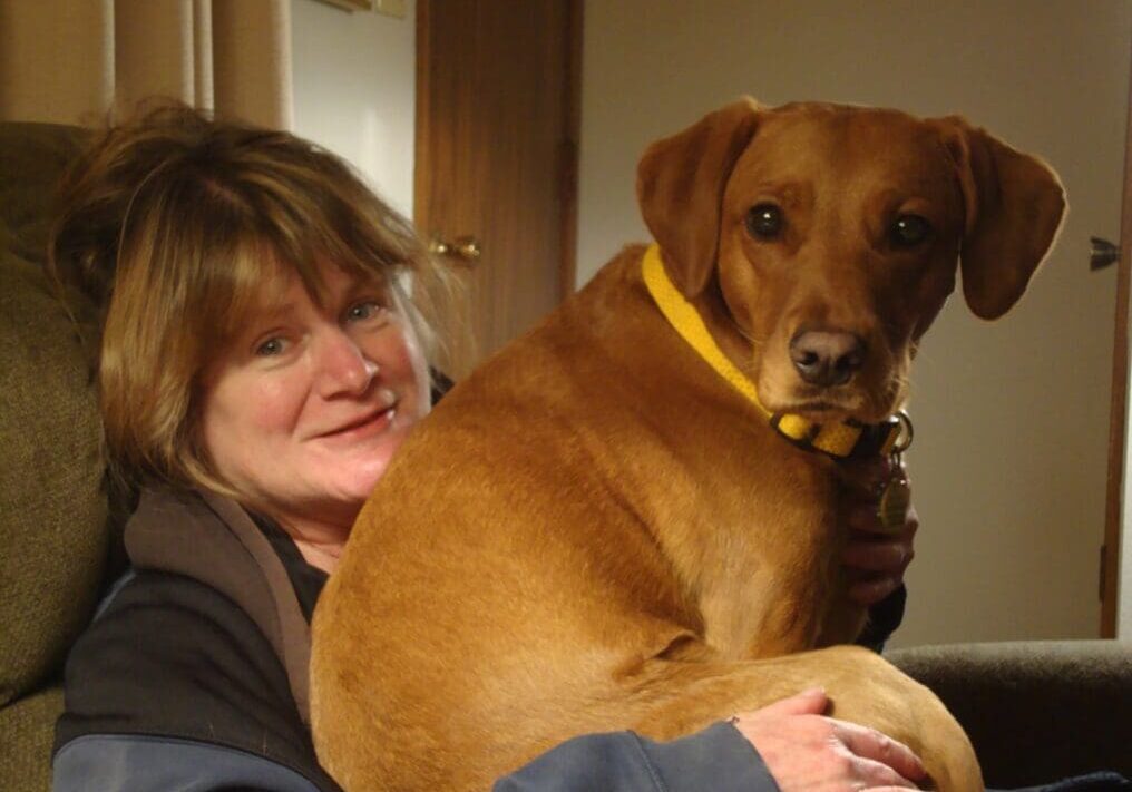 Woman smiling and hugging a brown dog.