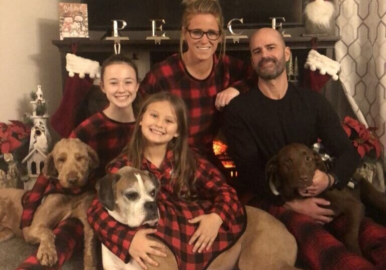 A family in plaid pajamas posing with their dogs.