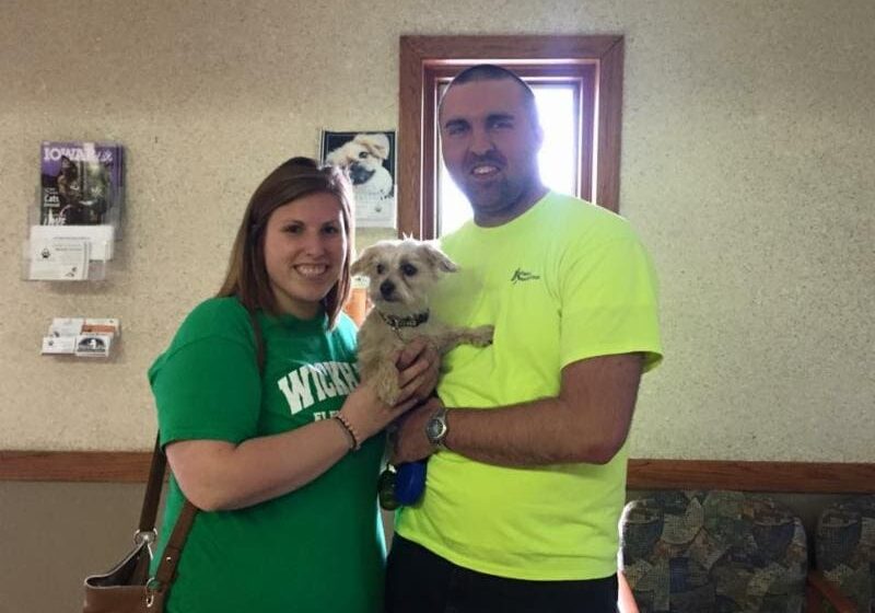 A man and woman posing with a dog in a waiting room.